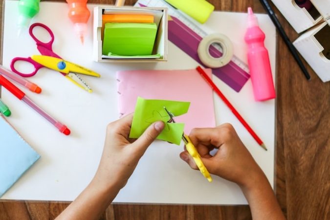 Des mains d'élève découpant avec soin une étoile en papier vert au milieu de fournitures scolaires colorées pour aménager une classe flexible avec un petit budget : guide pratique et astuces.