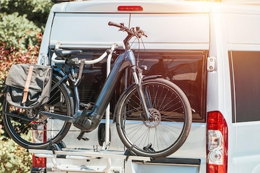 Un vélo électrique avec sacoche latérale fixé sur le porte-vélo arrière d'un bicycle camper stationné au soleil.