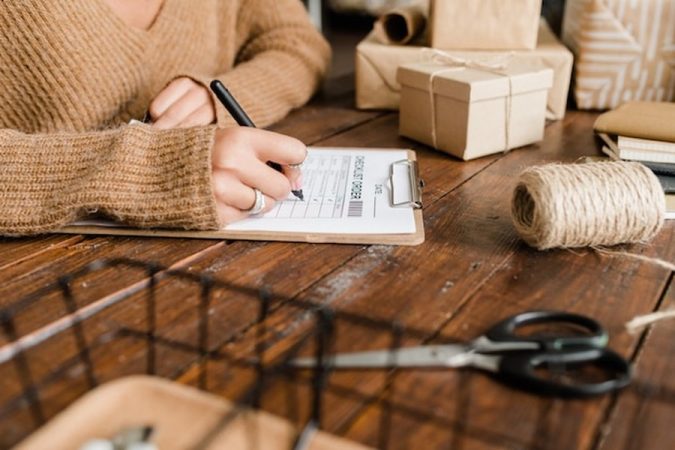 Une créatrice remplit un formulaire de commande sur un établi en bois pour calculer son prix de vente artisanal : la méthode mathématique pour ne plus vendre à perte.