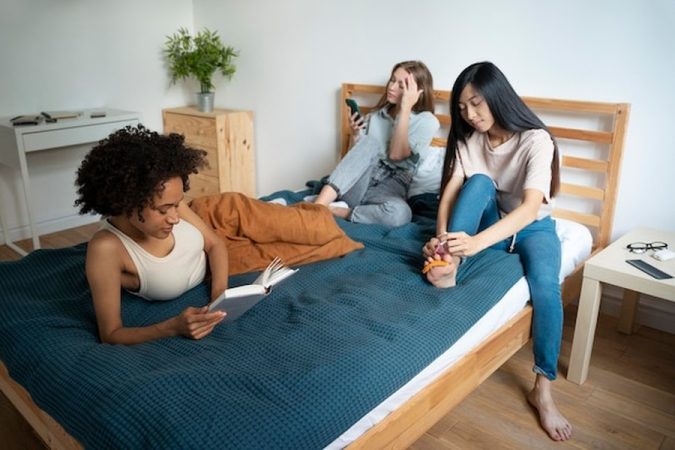 Trois jeunes femmes partagent un moment de détente et de convivialité dans une chambre, illustrant les bénéfices de la cohabitation intergénérationnelle solidaire : le guide complet pour loger un étudiant et réduire ses charges de moitié.