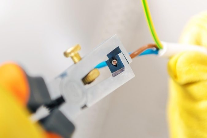 Un électricien utilise une pince à dénuder sur des fils électriques pour montrer comment ajouter une prise de terre sur une installation ancienne sans tout casser.