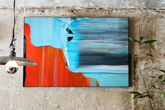 Un grand tableau abstrait aux nuances bleues et orangées sur un mur texturé, illustrant comment choisir la taille idéale d'un tableau pour son salon : la règle d'or des 4/7.