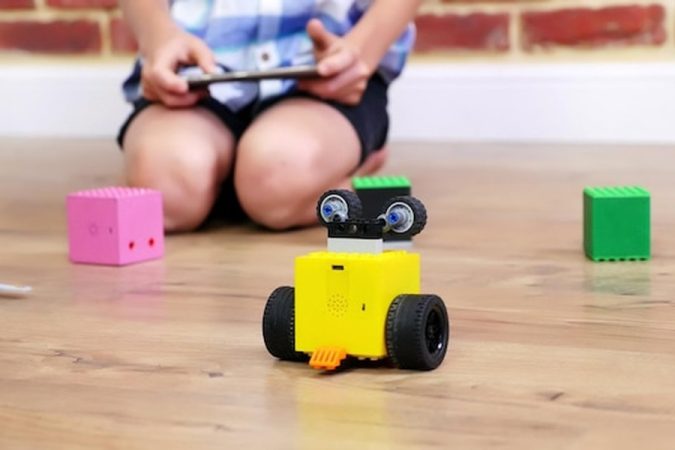 Un jeune enfant manipulant un petit robot jaune pour comprendre comment configurer le premier compagnon IA de votre enfant pour un éveil éducatif sans écrans en 2026.