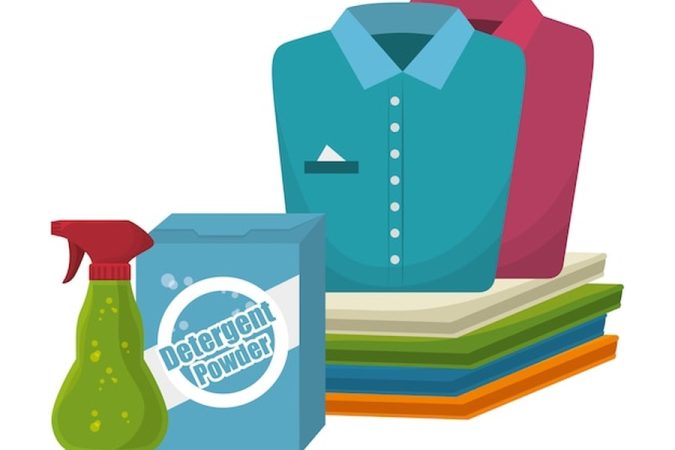 Une pile de linge propre accompagnée de produits de nettoyage pour savoir comment enlever une tache de gras ancienne sur un vêtement déjà lavé et séché.