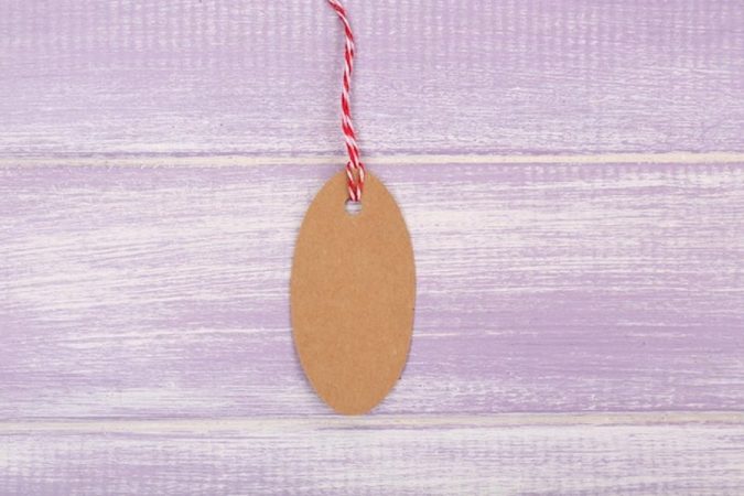 Une étiquette en kraft vierge avec une ficelle rouge et blanche posée sur du bois violet, illustrant comment fixer le prix de ses créations artisanales : la formule complète pour être enfin rentable.