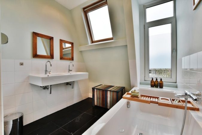 Une salle de bain moderne sous les toits avec une double vasque blanche et une baignoire lumineuse, illustrant parfaitement comment rénover une salle de bain sans casser le carrelage : solutions, étapes et budget.