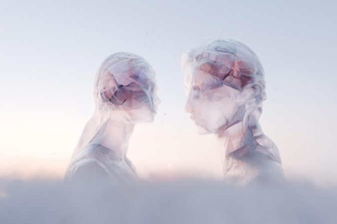 Deux profils éthérés et translucides se faisant face dans un univers vaporeux, illustrant comment savoir si quelqu'un pense à vous : 7 signes physiques de connexion télépathique.