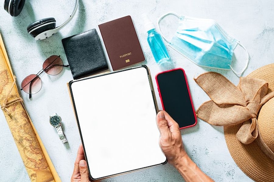 Une tablette numérique tenue au-dessus d'accessoires de voyage comme un passeport et un smartphone, illustrant le Digital Product Passport.