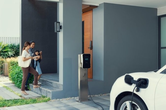 Une famille rentre chez elle pendant qu'un véhicule électrique se recharge, une mise en pratique concrète du Droit à la prise en copropriété : Le guide complet pour installer sa borne de recharge sans l'accord du syndic en 2024.