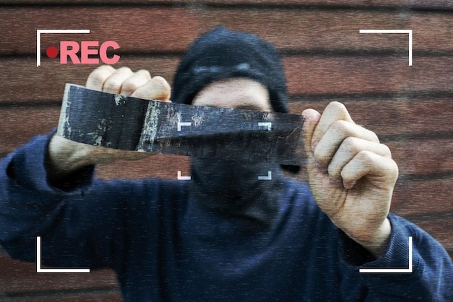 Un individu masqué manipulant du ruban adhésif devant une caméra pour créer une fake video evidence.