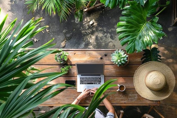 Une personne travaille sur un ordinateur portable depuis une terrasse exotique entourée de verdure, illustrant parfaitement les meilleures destinations 'Workation' à moins de 1000€ par mois : Le guide ultime pour télétravailler au soleil en 2024.