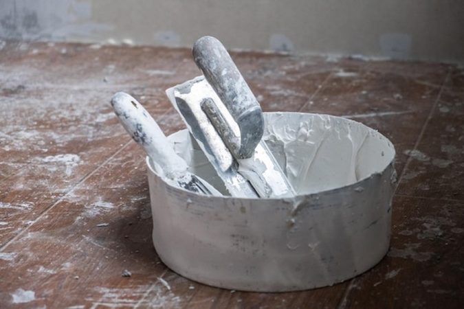 Outils de maçon et seau de mortier blanc prêts pour une Maçonnerie à la chaux sur mur en pierre : les 5 erreurs fatales qui détruisent votre façade.