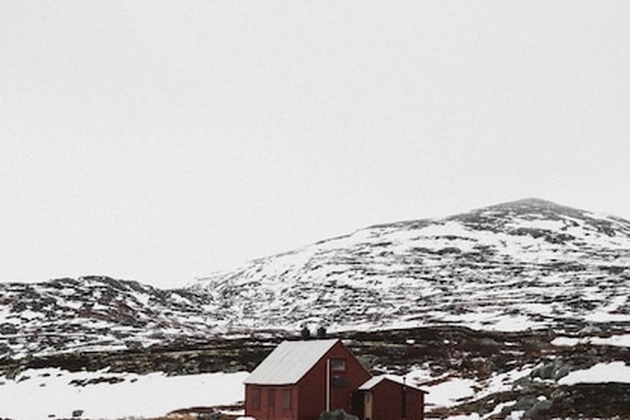 Une petite cabane rouge isolée au pied de montagnes enneigées dans un Nordic landscape épuré.