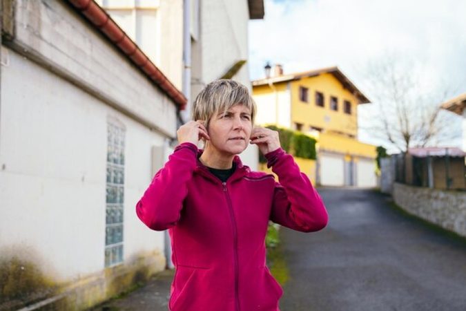 Une femme se bouche les oreilles dans une rue résidentielle pour illustrer les nuisances sonores de pompe à chaleur chez le voisin : Recours juridiques et guide pratique pour agir.