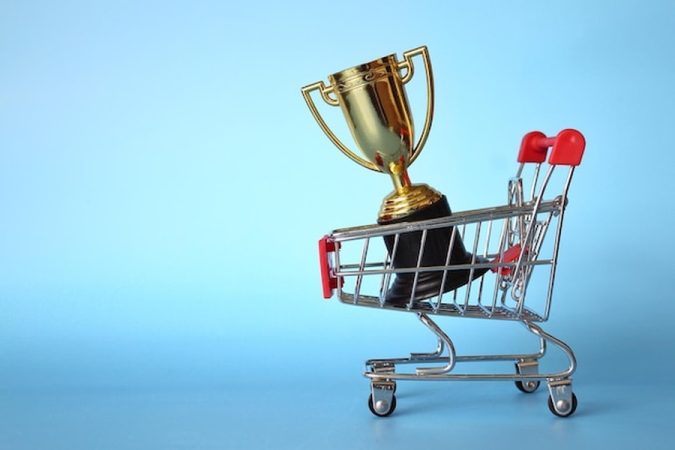 Un trophée doré posé dans un petit chariot de courses symbolisant la Publicité sur Retail Media : Comment les marques émergentes détrônent les géants sur les sites e-commerce.