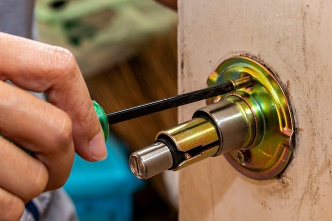 Une main utilisant un tournevis pour démonter un cylindre et réparer une Serrure 3 points bloquée porte ouverte : 5 étapes pour débloquer le mécanisme soi-même efficacement.