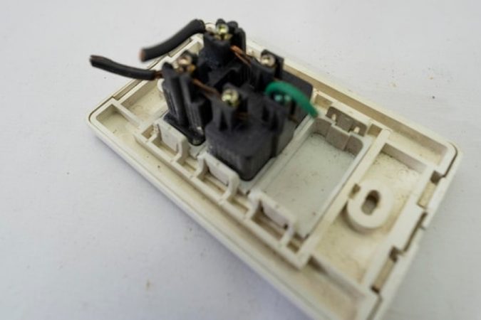 Arrière d'une prise de courant démontée montrant des fils mal serrés, un problème souvent lié au tableau électrique qui grésille ou siffle : causes, dangers et solutions.