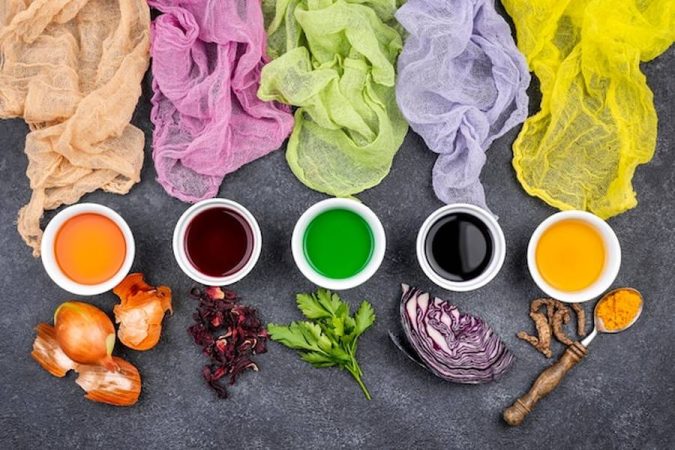 Des coupons de tissus aux nuances variées disposés au-dessus de bols de pigments extraits par teinture végétale : comment colorer vos tissus naturellement avec des déchets de cuisine (épluchures et noyaux).