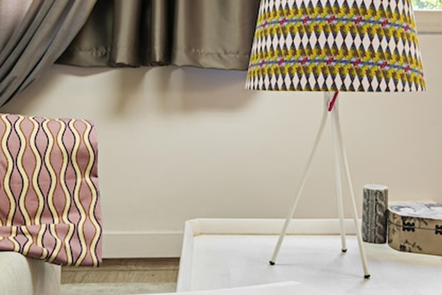 Un coin de pièce moderne avec une lampe trépied à motifs géométriques et des voilages satinés pour bien \choisir ses rideaux de salon 2026