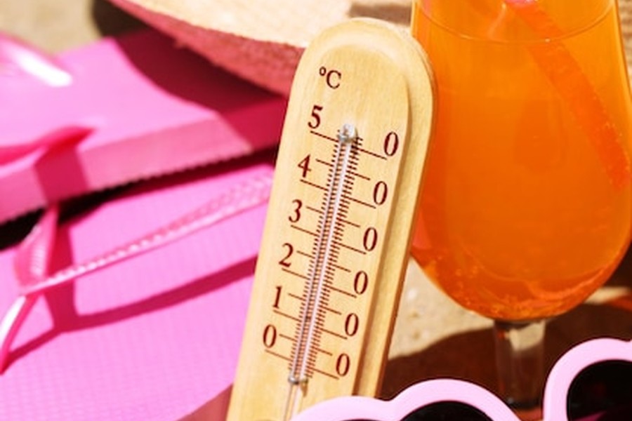 Un thermomètre en bois affichant une température dépassant les 40 degrés à côté de tongs roses, illustrant parfaitement le besoin de consulter le Guide de la Coolcation : Les meilleures destinations pour fuir la canicule cet été.