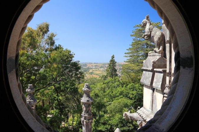 Un panorama verdoyant se dévoile à travers un oculus en pierre sculptée, illustrant parfaitement le Top 10 des 'Destination Dupes' en Europe : où partir pour éviter la foule et l'inflation en 2024.