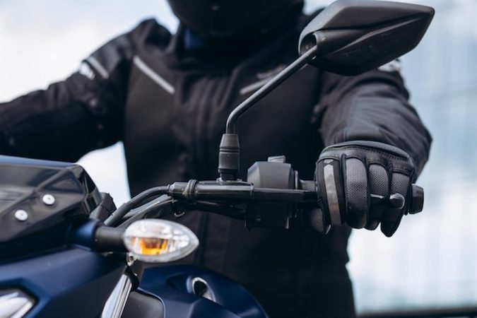 Un motard équipé de gants de protection tient le guidon de son véhicule, illustrant l'importance d'un Traceur GPS moto sans abonnement : le comparatif ultime pour protéger sa machine sans frais mensuels.