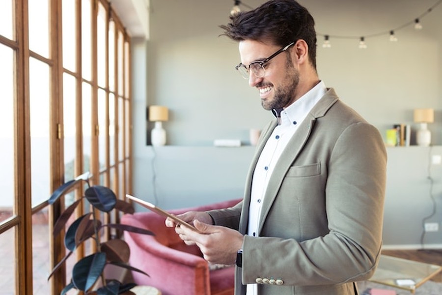 Un homme élégant sourit en consultant sa tablette pour savoir comment activer la garantie à vie de vos vêtements via le Passeport Numérique 2026.