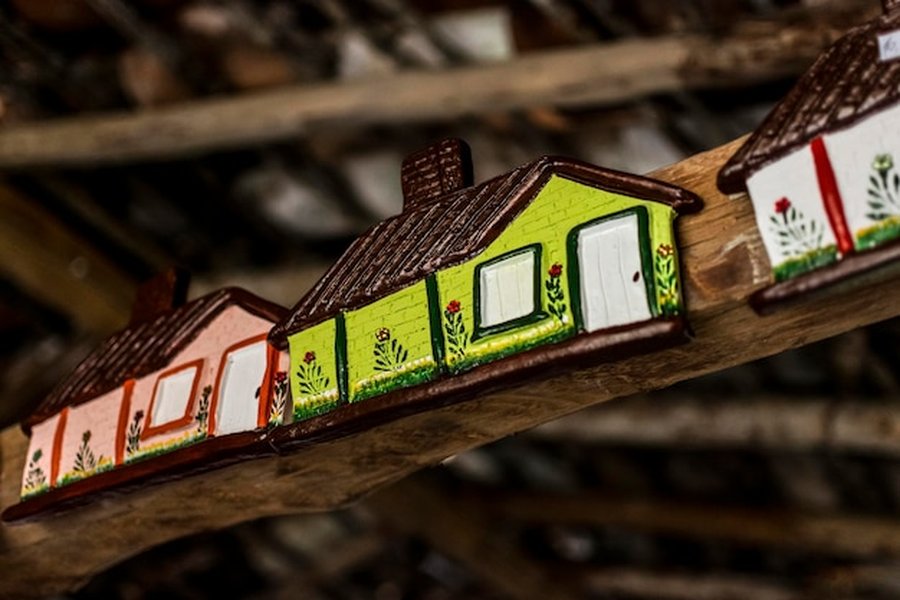 Petites maisons colorées artisanales fixées sur une poutre en bois pour illustrer les Normes DPE 2026 : comment isoler une maison ancienne par l'extérieur sans dénaturer la façade.