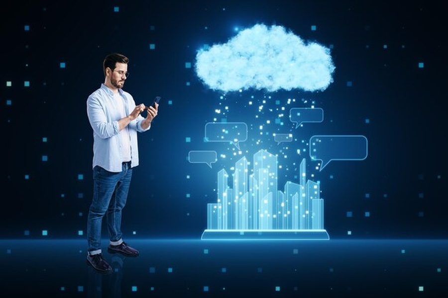 Un homme utilise son smartphone devant une interface holographique représentant une ville connectée et un nuage de données, illustrant comment héberger son propre agent IA autonome : la fin des abonnements Cloud.