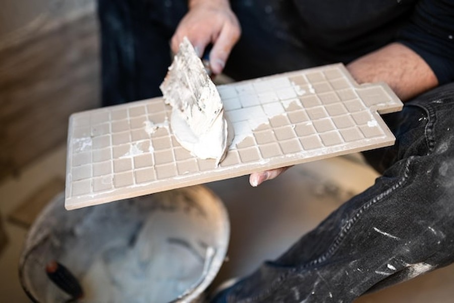 Un artisan étale une sous-couche d'accroche sur une chute de revêtement pour préparer la surface et comprendre comment appliquer une peinture à la chaux sur du carrelage : la méthode pour un rendu minéral sans tout casser.