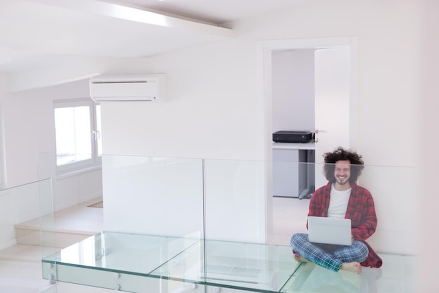 Un homme travaille sereinement sur son ordinateur dans un loft blanc et lumineux, une solution idéale pour comprendre comment créer une zone de fraîcheur passive en intérieur sans climatisation grâce à la conception bioclimatique.
