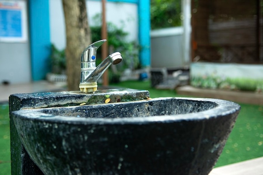 Un robinet en inox installé au-dessus d'une vasque en pierre noire dans un espace vert, illustrant le recyclage des eaux grises : comment réutiliser l'eau de la douche pour les WC et le jardin.