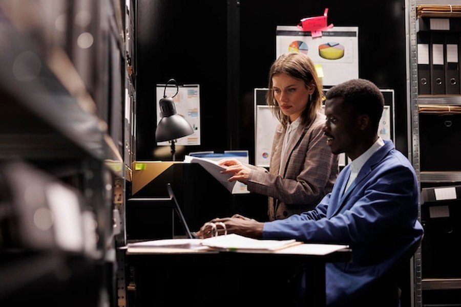 Deux professionnels analysant des dossiers stratégiques pour comprendre comment inscrire son entreprise dans les annuaires de sources pour les réponses de l'IA.