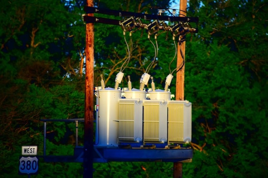 Transformateurs électriques sur poteaux devant une forêt dense, illustrant le réseau traditionnel et comment installer une batterie domestique au sel de mer pour atteindre l'autonomie énergétique.