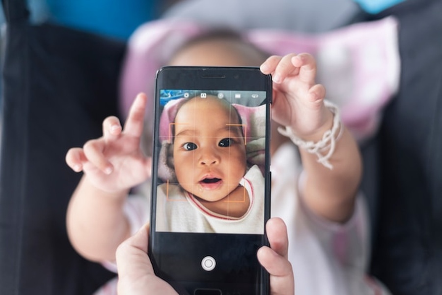 Un smartphone capture le visage d'un nouveau-né dans sa poussette, illustrant les enjeux de l'identité numérique de bébé : comment sécuriser ses données et éviter le sharenting.