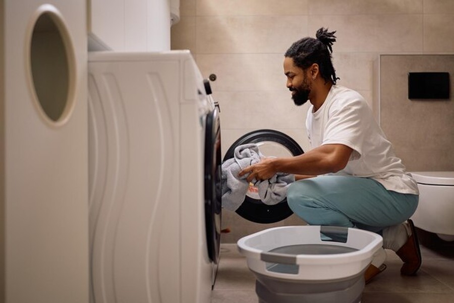 Un homme utilise sa machine à laver dans une buanderie moderne, une étape clé quand on cherche comment installer un système de recyclage des eaux grises pour alimenter ses WC et son lave-linge.