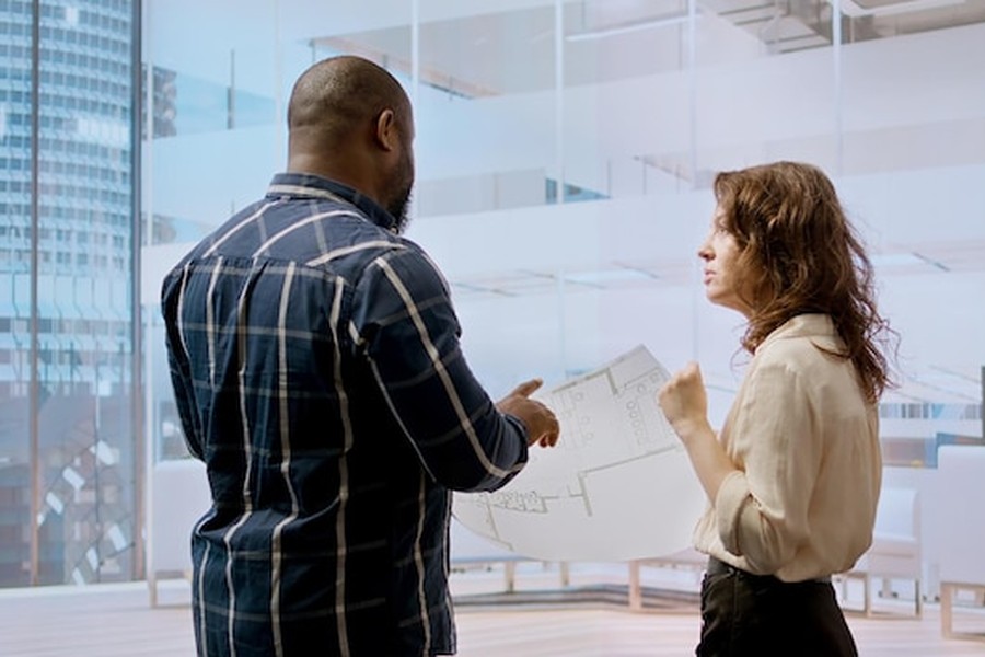 Un homme et une femme analysent des plans techniques dans un bureau moderne, illustrant les étapes pour récupérer son rapport d'évaluation IA après un entretien manqué.