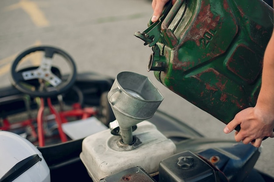 Un jerrycan en métal vert alimente un moteur via un entonnoir, une solution concrète pour les carburants de synthèse (e-fuels) pour moto : compatibilité moteur et avenir du thermique.