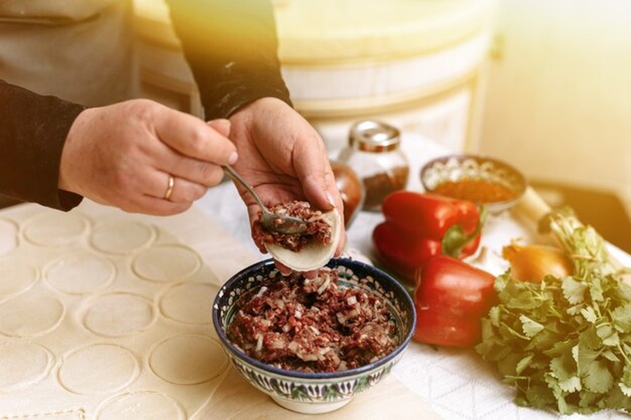 Un cuisinier dépose une farce de bœuf haché et d'oignons dans un disque de pâte fine, illustrant parfaitement comment utiliser le koji pour maturer votre viande à la maison en 48 heures.