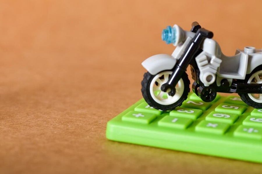 Une moto miniature grise posée sur une calculatrice verte pour calculer le nouveau malus écologique et la taxe sur la masse des motos de 2026.