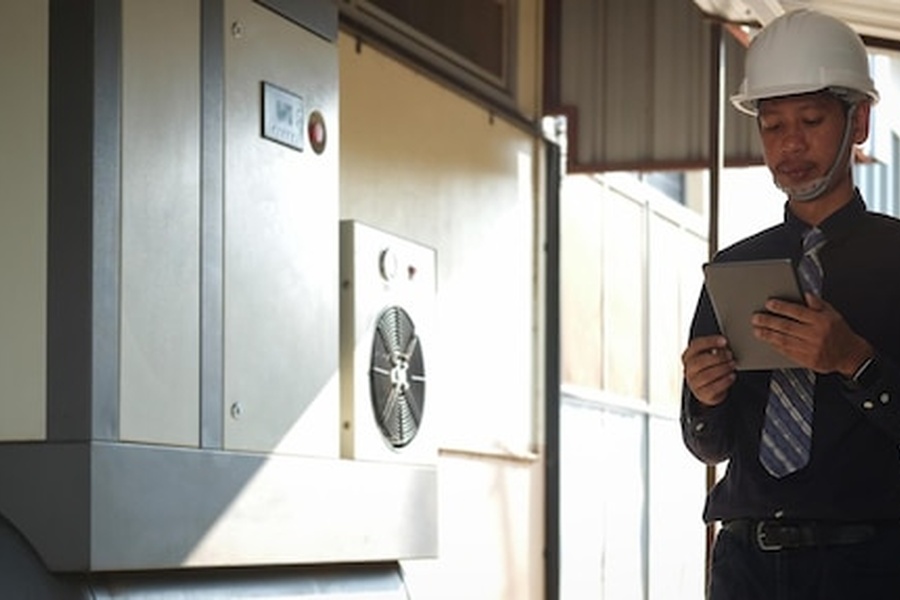 Un technicien qualifié utilise une tablette numérique pour installer un récupérateur de chaleur sur eaux grises : le guide pour réduire sa facture d'eau chaude devant un équipement thermique.