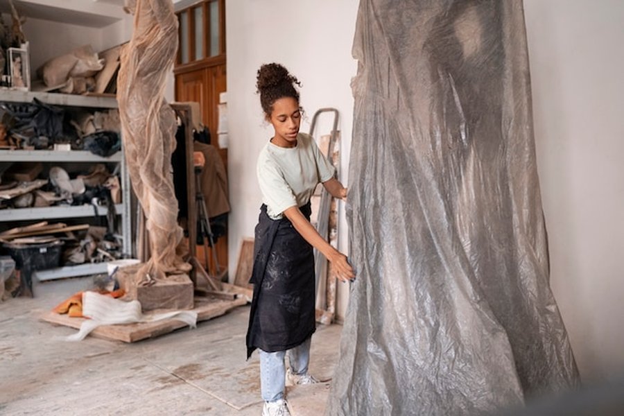 Une artisane manipule des bâches de protection dans son atelier, illustrant la phase de préparation d'une Rénovation circulaire : comment sourcer et réutiliser des matériaux de réemploi pour son intérieur.