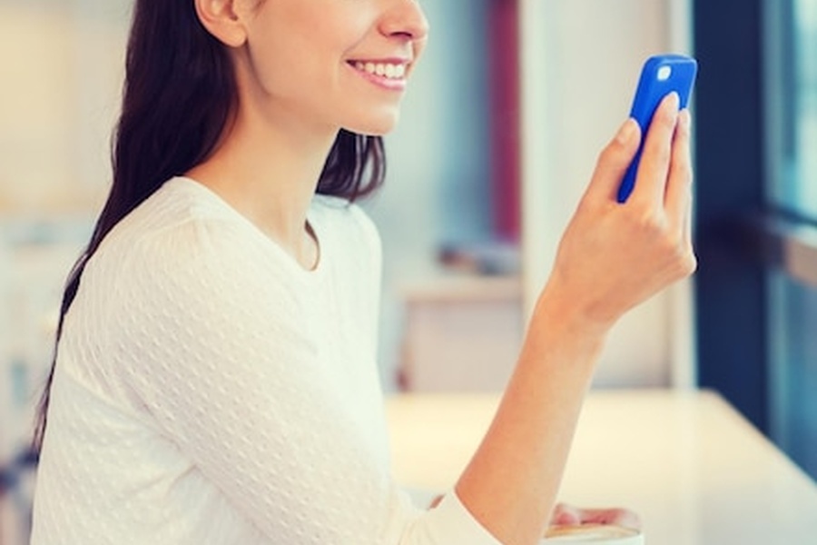 Une femme souriante consulte son smartphone pour atteindre un nouveau palier d'endurance en gérant son glucose sanguin en temps réel.