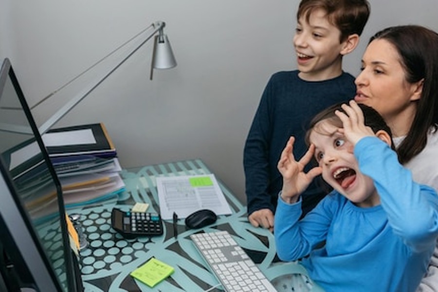 Une mère et ses deux enfants s'amusant devant un écran d'ordinateur pour apprendre à créer un 'safe word' familial pour déjouer les tentatives d'extorsion par clone vocal.