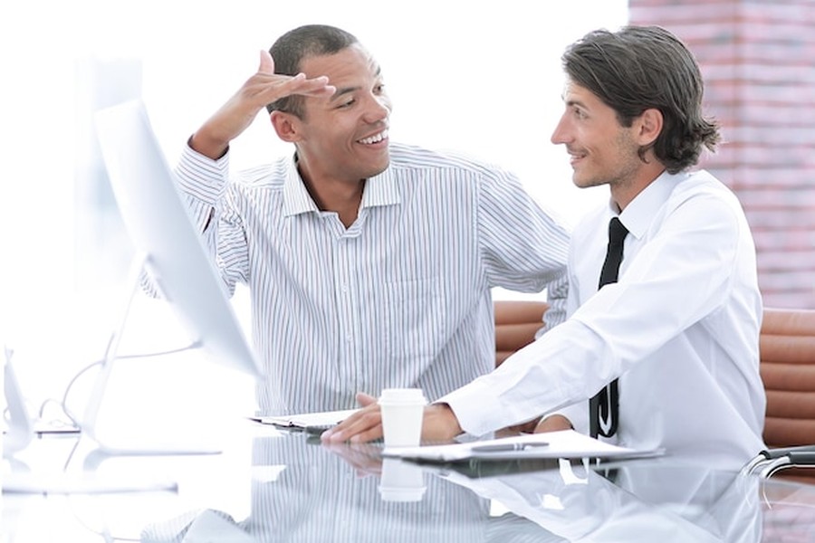 Deux collaborateurs de bureau discutant de comment récupérer deux fois plus vite grâce à la stimulation neuro-musculaire pilotée par IA devant leur poste de travail.