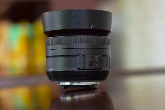 Objectif d'appareil photo noir équipé d'un pare-soleil, posé sur une surface sombre réfléchissante.