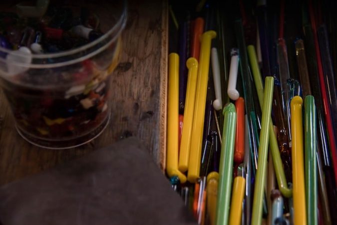 Des tiges de verre coloré et des éclats multicolores disposés sur un établi, parfaits pour ajouter du relief à une peinture pour acrylique.