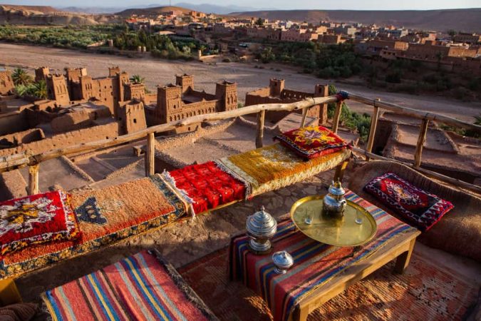 Terrasse traditionnelle avec tapis berbères et service à thé surplombant les kasbahs en terre cuite, idéale pour un voyage au Maroc authentique