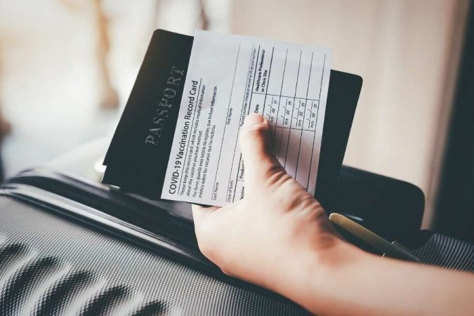 Une main tenant un passeport et des documents de voyage officiels posés sur une valise de voyage.