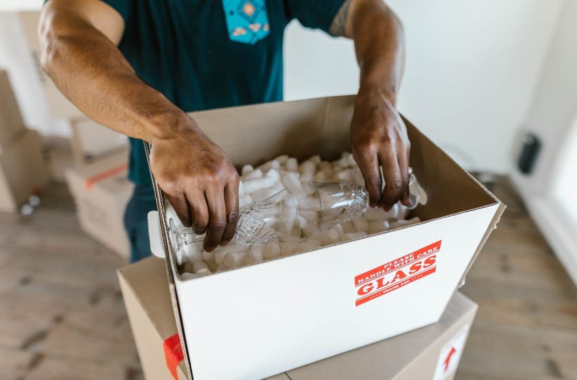 Un homme place délicatement de la vaisselle en cristal dans des particules de calage, illustrant la technique pour emballer des verres à pied dans un carton de déménagement